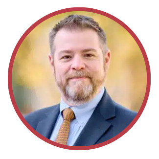 Professional headshot of UMC President & CEO Mark Lenhard. Mark wears a blue shirt and jacket in an outdoor setting.