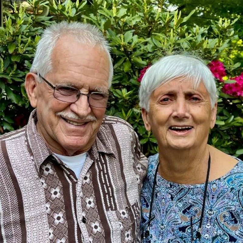 Man and woman UMCF supporters standing in front of a flowering bush.