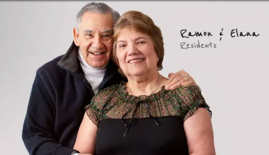 An older man and woman in black tops smile for the camera during a photo shoot at their UMC senior living community.