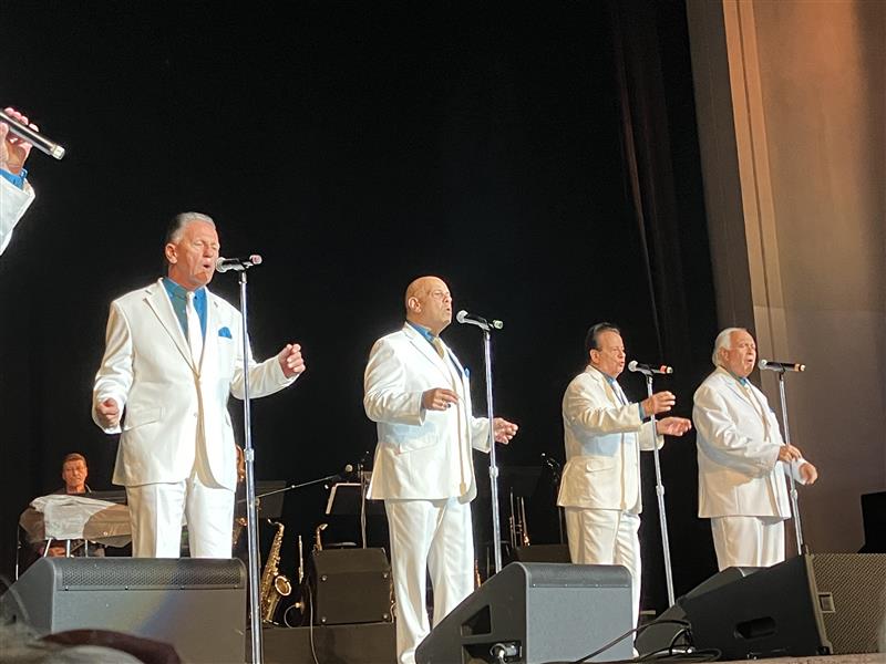 Four men in white suits singing on stage
